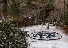 a fire pit surrounded by chairs and lights in the middle of a snow covered forest