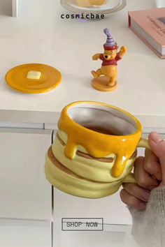 a person holding a yellow mug with a bear on it in front of a counter