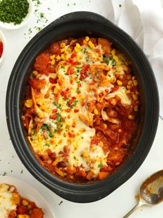 a crock pot filled with meat and vegetables covered in sauce, cheese and herbs