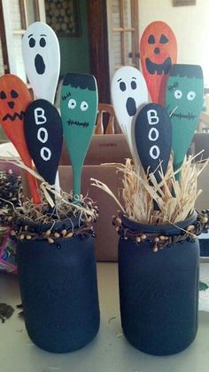 four halloween wooden spoons with faces on them are sitting in a blue vase filled with hay