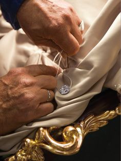 the hands of a man who is stitching something on a cloth with scissors and thread