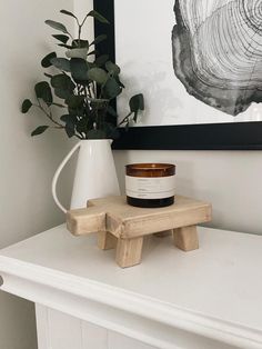 a candle on a wooden stool next to a potted plant in a white vase