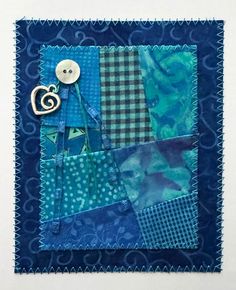 a blue patchwork quilt with a button on the center and a heart in the middle