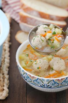 a spoon full of soup with meatballs and carrots in it next to bread