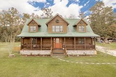 a large log cabin with a green roof and two porches on the front lawn