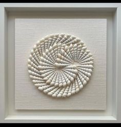 a white framed art piece with shells in it's center and an intricate design on the bottom