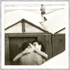 an old photo of two people hugging each other in front of some tents on the beach