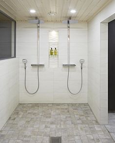 two shower heads in the middle of a tiled floored bathroom with white walls and ceiling