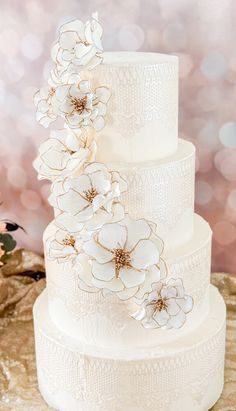 a wedding cake with white flowers on top is sitting on a table in front of some lights