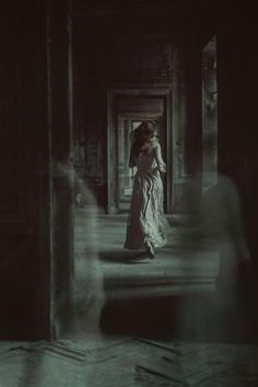 a woman in a long dress walking through a dark room with her back to the camera