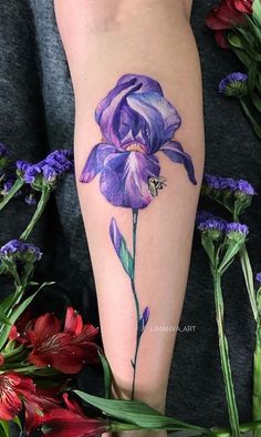 a woman's leg with a purple flower tattoo on her left arm and flowers in the background