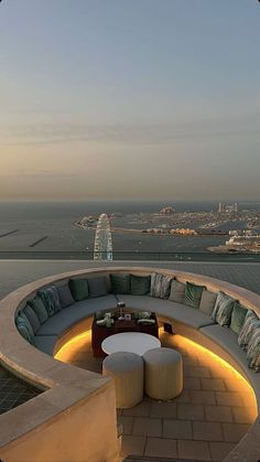 an outdoor seating area overlooking the ocean and city skyline at dusk with lights on it