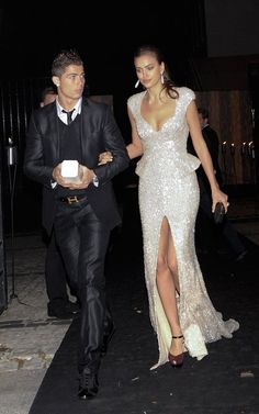 a man and woman dressed in formal wear walking down the street at night with one holding an object