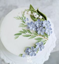 a white cake decorated with blue flowers and green leaves