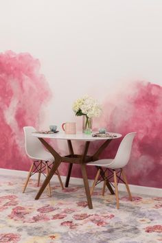 a dining room table with two chairs and a vase on top of it in front of a pink painted wall