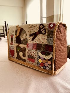 a purse made out of fabric and buttons on a table with chairs in the background