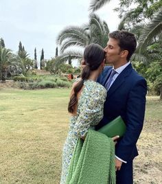 a man in a suit and tie kissing a woman on the cheek with palm trees behind them