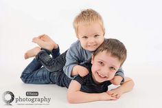 two young boys laying on the ground with their arms around each other and smiling at the camera