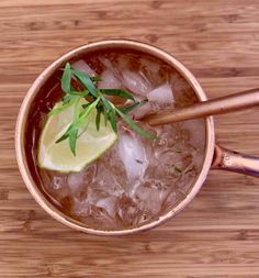 a cup filled with ice and lime on top of a wooden table next to a spoon