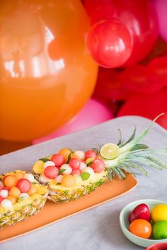 two pineapples on a plate with fruit in the middle and balloons behind them