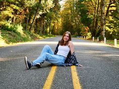 a woman sitting on the side of a road with her legs crossed and smiling at the camera