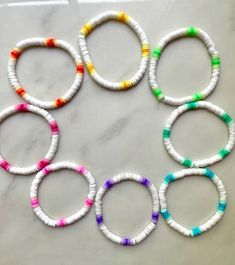 six bracelets made out of white paper with multicolored beads on top of a marble surface