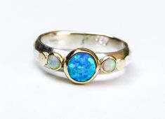 a ring with three opal stones in it on a white surface, one is gold and the other is silver