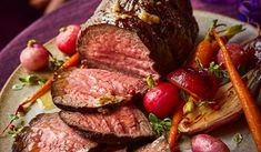 a plate with meat, potatoes and carrots on it next to a purple table cloth