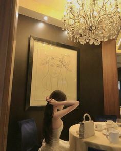 a woman in a white dress is sitting at a table with a chandelier