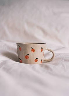 a coffee cup sitting on top of a white bed covered in sheets and pillows with an orange print