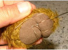 a person holding a needle and thread in their hand with a stuffed animal on it