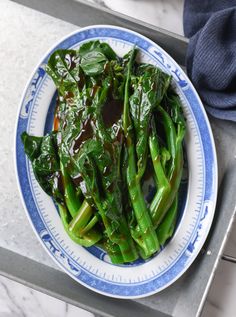 a blue and white plate topped with green vegetables on top of a counter next to a napkin