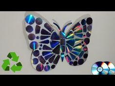 a butterfly made out of cds sitting on top of a white table next to a green recycle