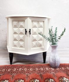 a white cabinet sitting on top of a rug next to a vase with a plant