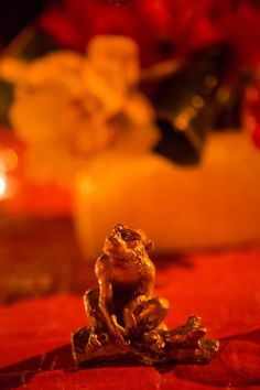 a gold frog figurine sitting on top of a red table cloth next to candles