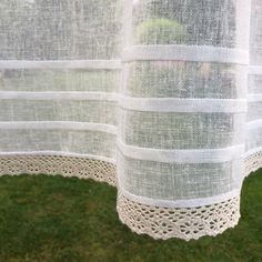 two white sheer curtains hanging from the side of a building with grass in front of them