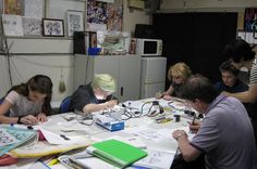 a group of people sitting around a table working on some paper and wires in front of them