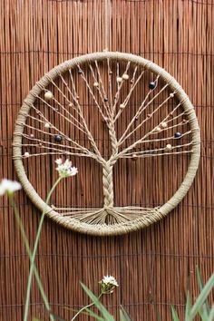 a wicker wall hanging with a tree on it and flowers in the foreground