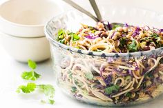 a glass bowl filled with noodles and veggies next to a small white bowl