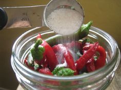 a glass jar filled with red and green peppers next to a measuring cup full of sugar