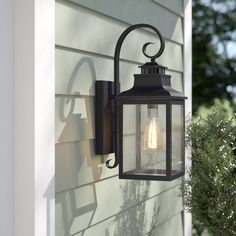 an outdoor wall light on the side of a house next to a bush and shrubbery