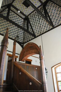 an ornate wooden staircase with blue and white wallpaper on the ceiling, along with wood handrails