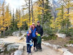 three people standing on a trail in the mountains with trees and rocks around them, one person is holding a frisbee