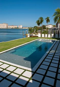 an empty swimming pool in the middle of a lawn area next to a body of water