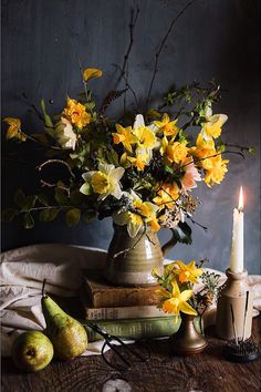 a vase filled with yellow flowers sitting on top of a table next to two pears