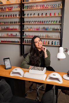 a woman sitting at a desk in front of a display of nail polish