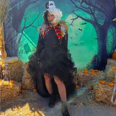 a woman in a black dress sitting on hay with pumpkins around her and a painting behind her