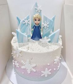 a frozen princess cake with white frosting and blue icing on the top is surrounded by snowflakes