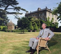 a man in a suit sitting on a chair outside an old house with trees and grass