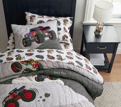 a bed with monster trucks on it and a night stand next to the bedding